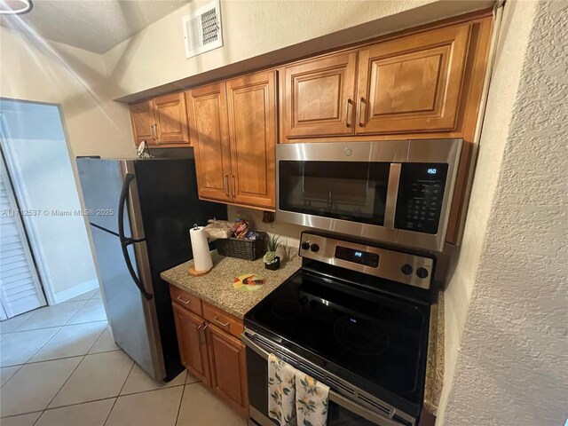 kitchen with light stone counters, stainless steel appliances, and light tile patterned floors