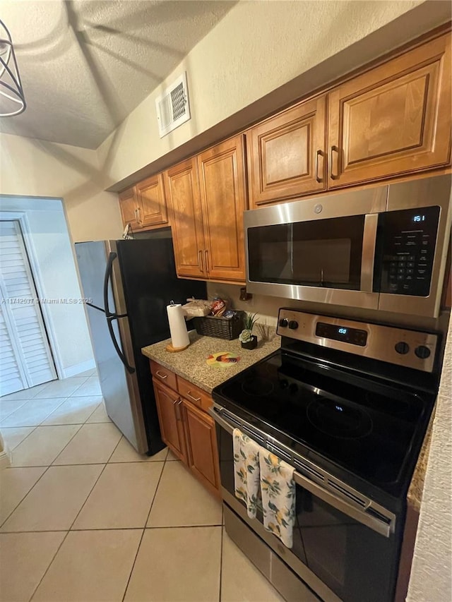 kitchen with stainless steel appliances, light tile patterned floors, a textured ceiling, and light stone counters