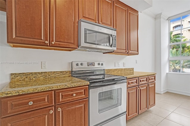 kitchen featuring light stone countertops, light tile patterned floors, ornamental molding, and appliances with stainless steel finishes