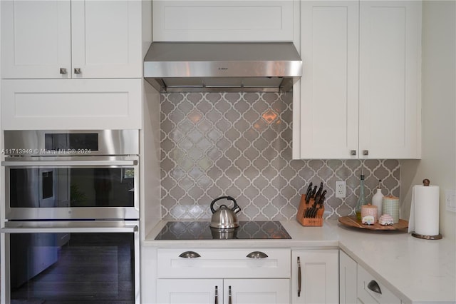 kitchen with wall chimney exhaust hood, stainless steel double oven, tasteful backsplash, black electric cooktop, and white cabinets