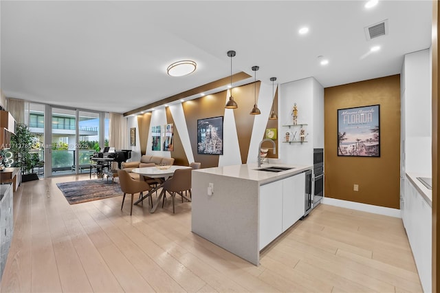 kitchen with sink, white cabinets, hanging light fixtures, light hardwood / wood-style floors, and kitchen peninsula