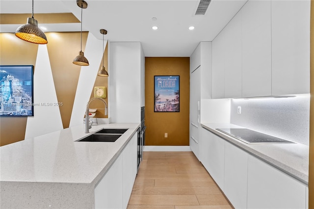 kitchen with sink, hanging light fixtures, black electric stovetop, white cabinets, and light wood-type flooring