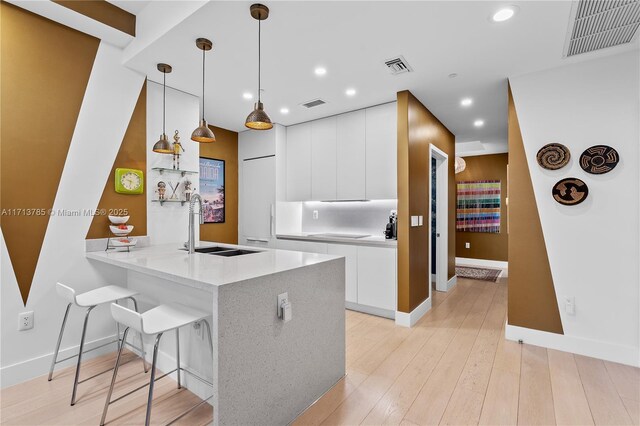 kitchen with sink, white cabinetry, decorative light fixtures, kitchen peninsula, and light wood-type flooring