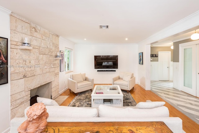 living room with light hardwood / wood-style floors, a stone fireplace, and crown molding