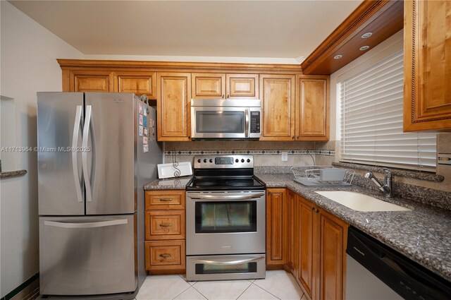 kitchen featuring dark stone counters, sink, decorative backsplash, light tile patterned floors, and appliances with stainless steel finishes