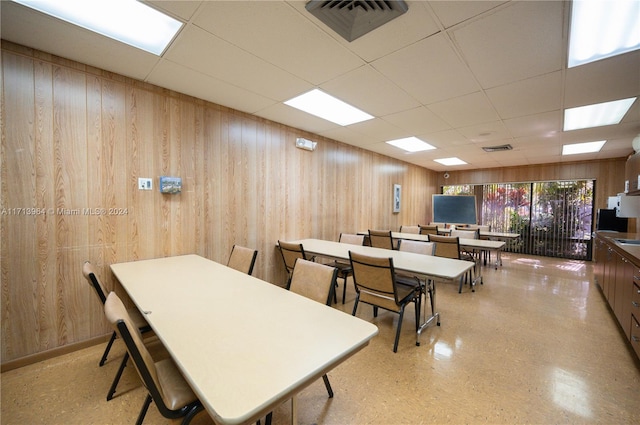 dining area with wooden walls and a drop ceiling