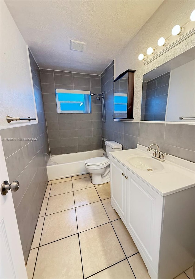 full bathroom featuring vanity, tiled shower / bath, a textured ceiling, and tile walls