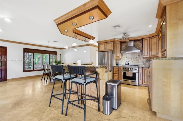 kitchen featuring appliances with stainless steel finishes, light stone counters, a breakfast bar, ceiling fan, and wall chimney range hood