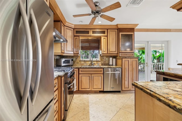 kitchen with stone counters, appliances with stainless steel finishes, wall chimney exhaust hood, and sink