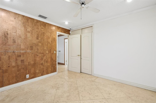 unfurnished bedroom with ceiling fan, wood walls, ornamental molding, and a closet