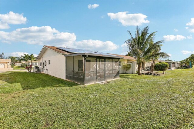 rear view of house with central AC unit, a yard, a sunroom, and solar panels