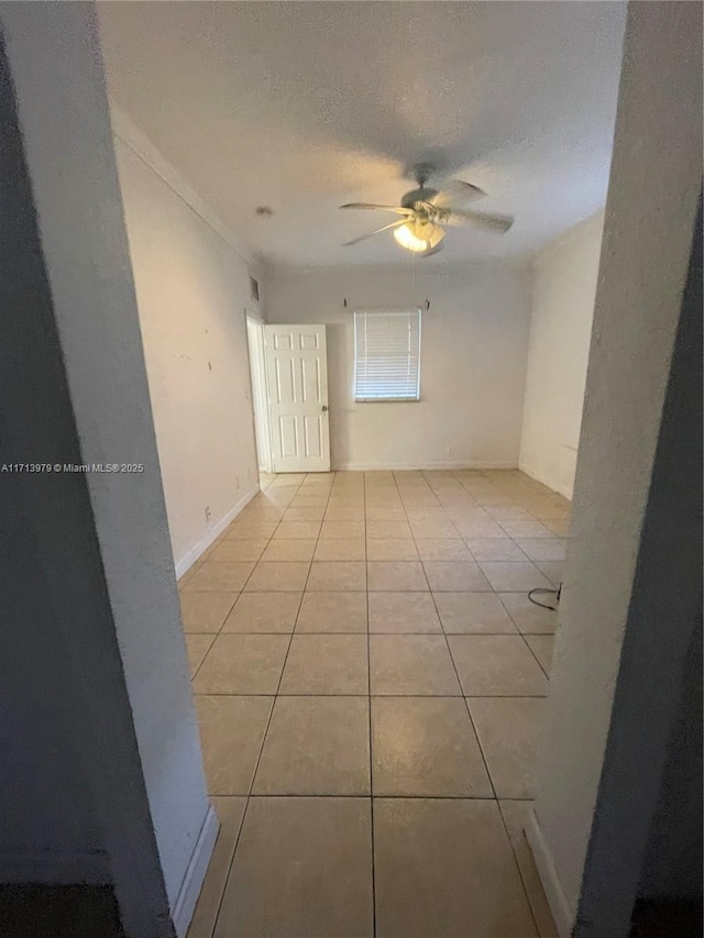 empty room featuring a textured ceiling, ceiling fan, and light tile patterned flooring