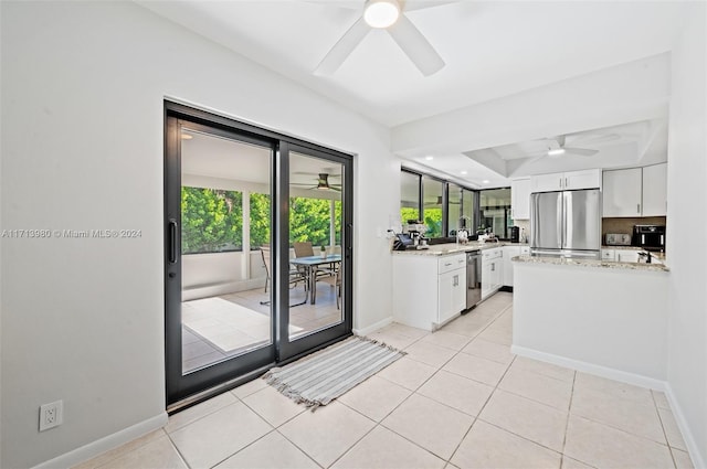 kitchen with white cabinets, a tray ceiling, stainless steel appliances, light stone counters, and light tile patterned floors