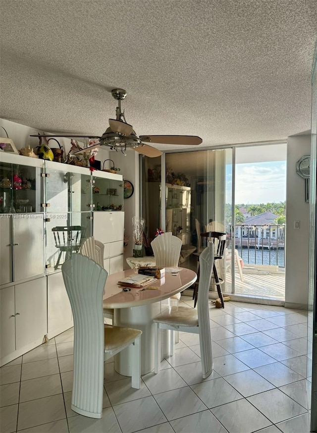 tiled dining space with a water view, a wall of windows, and ceiling fan