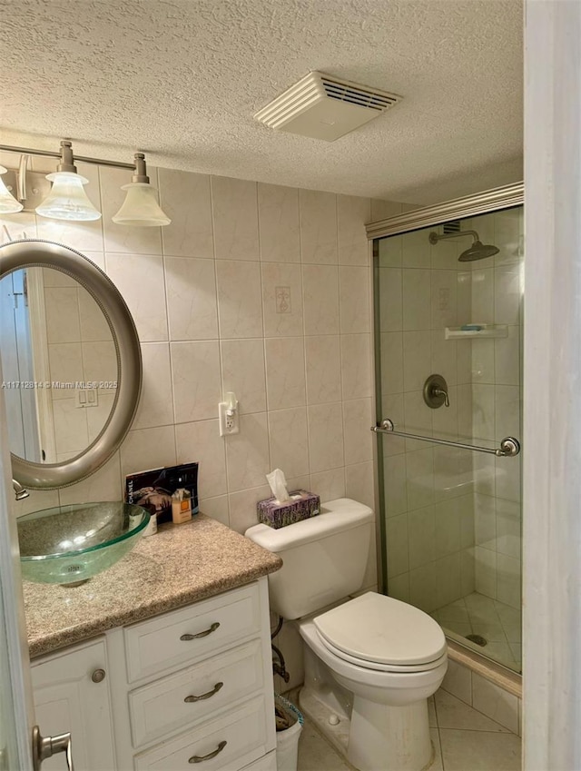 bathroom with vanity, a shower with shower door, a textured ceiling, and tile walls