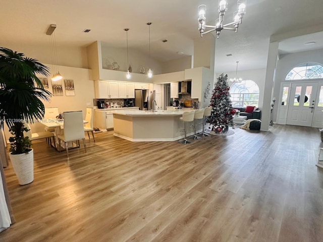 kitchen with pendant lighting, white cabinets, wall chimney range hood, decorative backsplash, and a notable chandelier