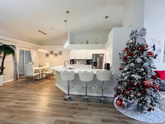 kitchen with decorative backsplash, stainless steel refrigerator with ice dispenser, high vaulted ceiling, white cabinets, and hanging light fixtures