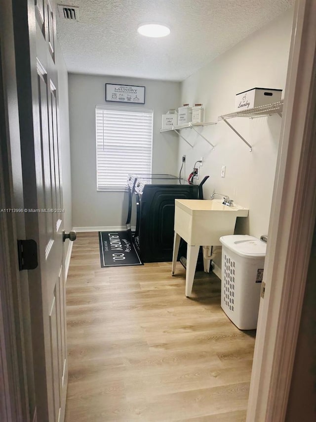 laundry area featuring washing machine and dryer, a textured ceiling, and light hardwood / wood-style flooring