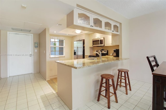 kitchen with a kitchen breakfast bar, light stone countertops, light tile patterned flooring, kitchen peninsula, and stainless steel appliances