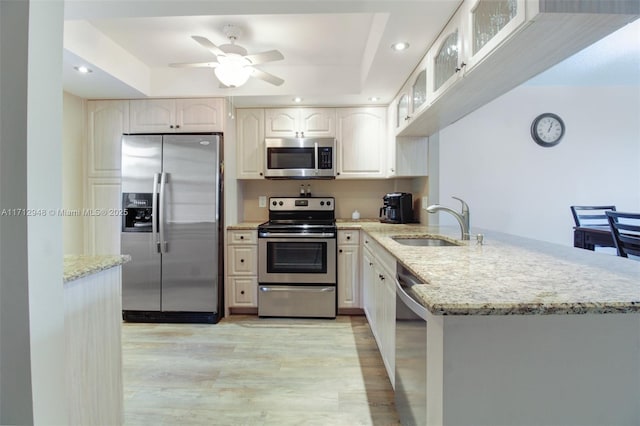 kitchen featuring appliances with stainless steel finishes, a peninsula, a sink, glass insert cabinets, and light stone counters