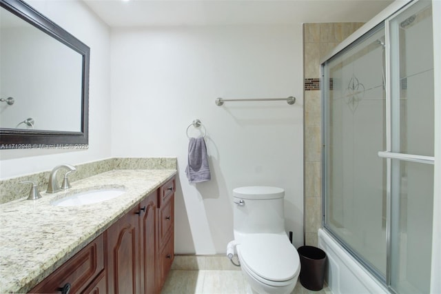 bathroom featuring toilet, vanity, shower / bath combination with glass door, and baseboards