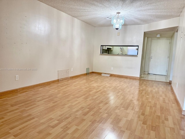 spare room with light wood-style flooring, a notable chandelier, and a textured ceiling