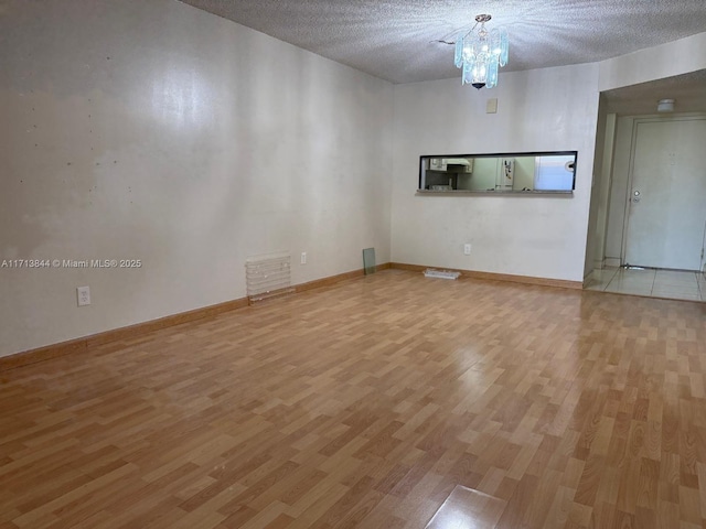 empty room featuring baseboards, visible vents, light wood finished floors, a textured ceiling, and a chandelier