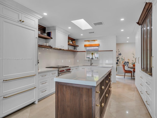 kitchen featuring white cabinets, a kitchen island, stainless steel stove, and a skylight