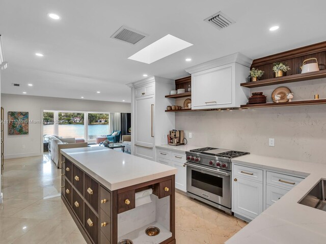 kitchen featuring a skylight, a center island, luxury range, light stone counters, and white cabinets