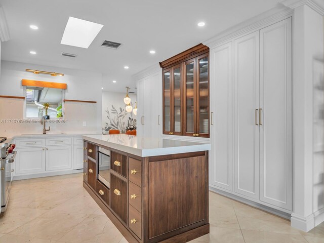 kitchen featuring a skylight, built in microwave, sink, a kitchen island, and white cabinets