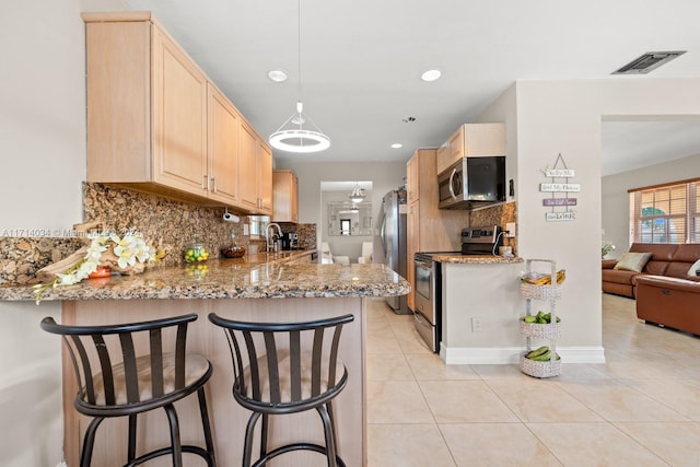 kitchen featuring a breakfast bar, stainless steel appliances, tasteful backsplash, kitchen peninsula, and light brown cabinetry