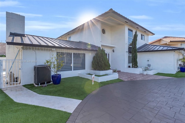 view of front of home featuring a patio, metal roof, a standing seam roof, a front lawn, and stucco siding