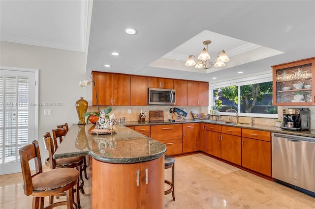 kitchen with appliances with stainless steel finishes, brown cabinetry, a raised ceiling, and a kitchen breakfast bar