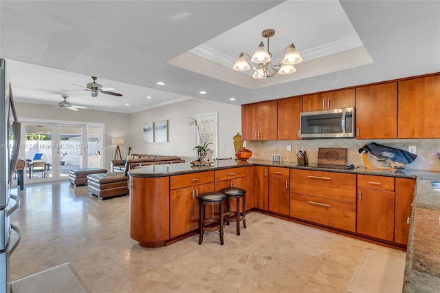 kitchen with a tray ceiling, stainless steel microwave, and brown cabinetry