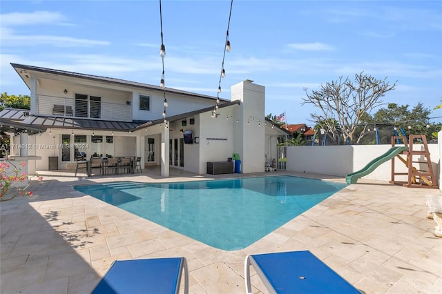 view of pool with a fenced in pool, a playground, a patio, outdoor dry bar, and a water slide