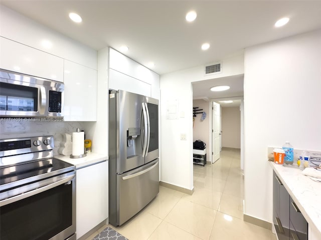 kitchen with light stone countertops, white cabinetry, light tile patterned floors, and stainless steel appliances