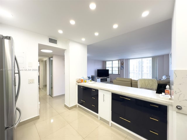 kitchen with stainless steel fridge, light tile patterned flooring, and light stone counters