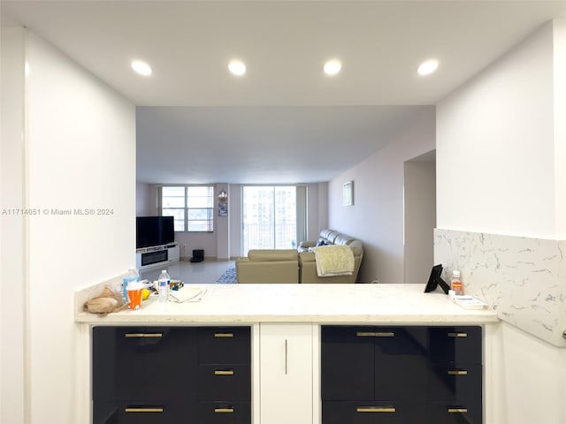 kitchen featuring white cabinetry, backsplash, light stone countertops, and kitchen peninsula