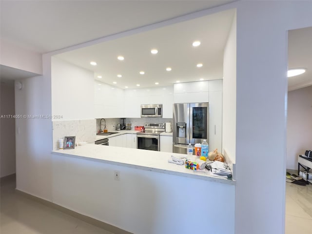 kitchen with sink, stainless steel appliances, tasteful backsplash, kitchen peninsula, and white cabinets