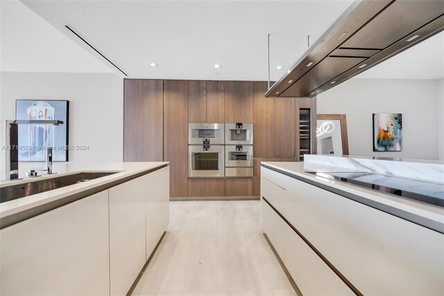 kitchen featuring white cabinets, ventilation hood, stainless steel double oven, and sink