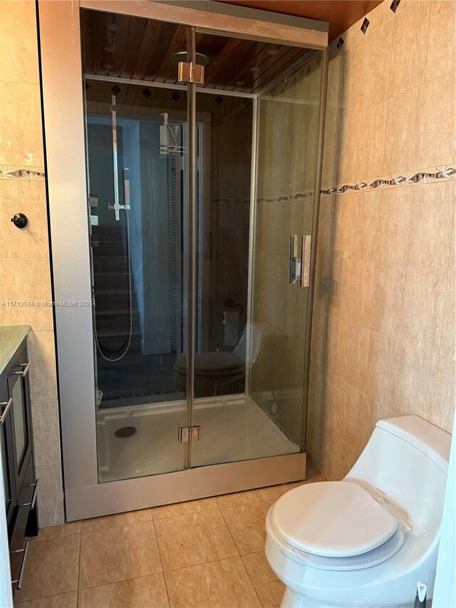 bathroom featuring tile patterned flooring, toilet, vanity, a shower with shower door, and tile walls