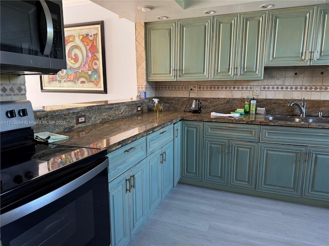 kitchen with sink, black range with electric cooktop, dark stone counters, decorative backsplash, and light wood-type flooring