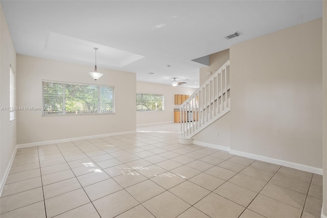 empty room featuring a tray ceiling, ceiling fan, and light tile patterned flooring