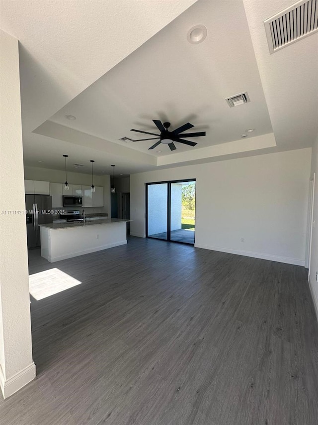 unfurnished living room featuring a raised ceiling, ceiling fan, dark hardwood / wood-style flooring, and sink