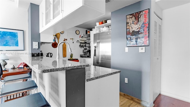 kitchen featuring white cabinets, dark stone countertops, stainless steel fridge with ice dispenser, and kitchen peninsula