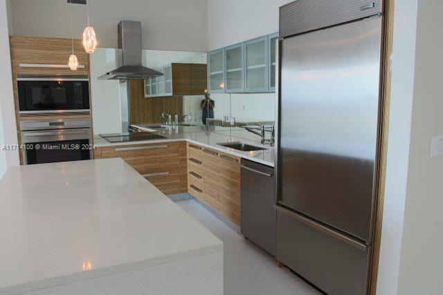 kitchen with pendant lighting, sink, stainless steel appliances, and wall chimney range hood