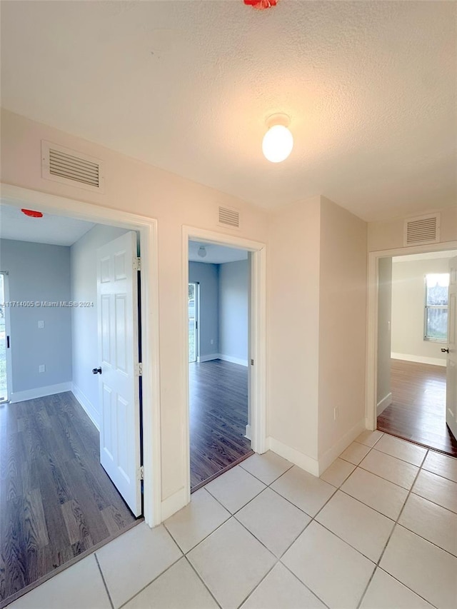 hallway with light tile patterned floors, a textured ceiling, and a wealth of natural light