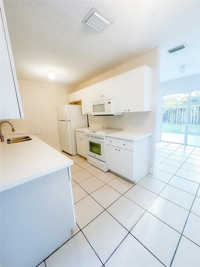 kitchen with white appliances, a textured ceiling, sink, light tile patterned floors, and white cabinets