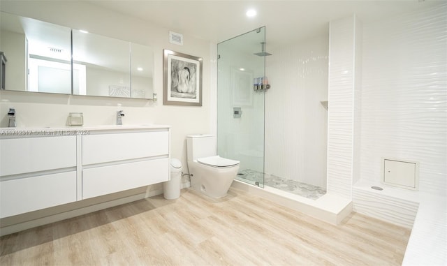 bathroom with tiled shower, wood-type flooring, vanity, and toilet