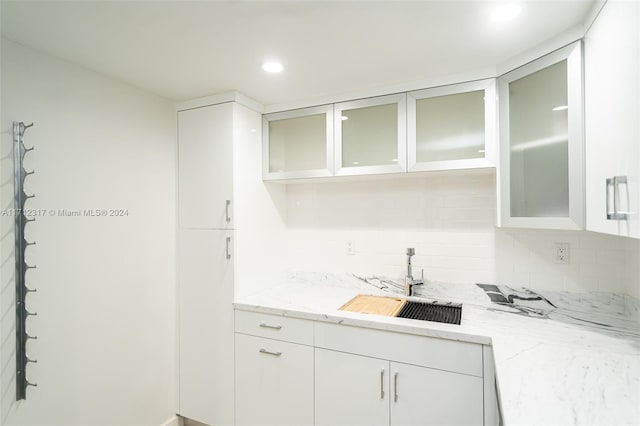 kitchen featuring white cabinets, tasteful backsplash, light stone counters, and sink